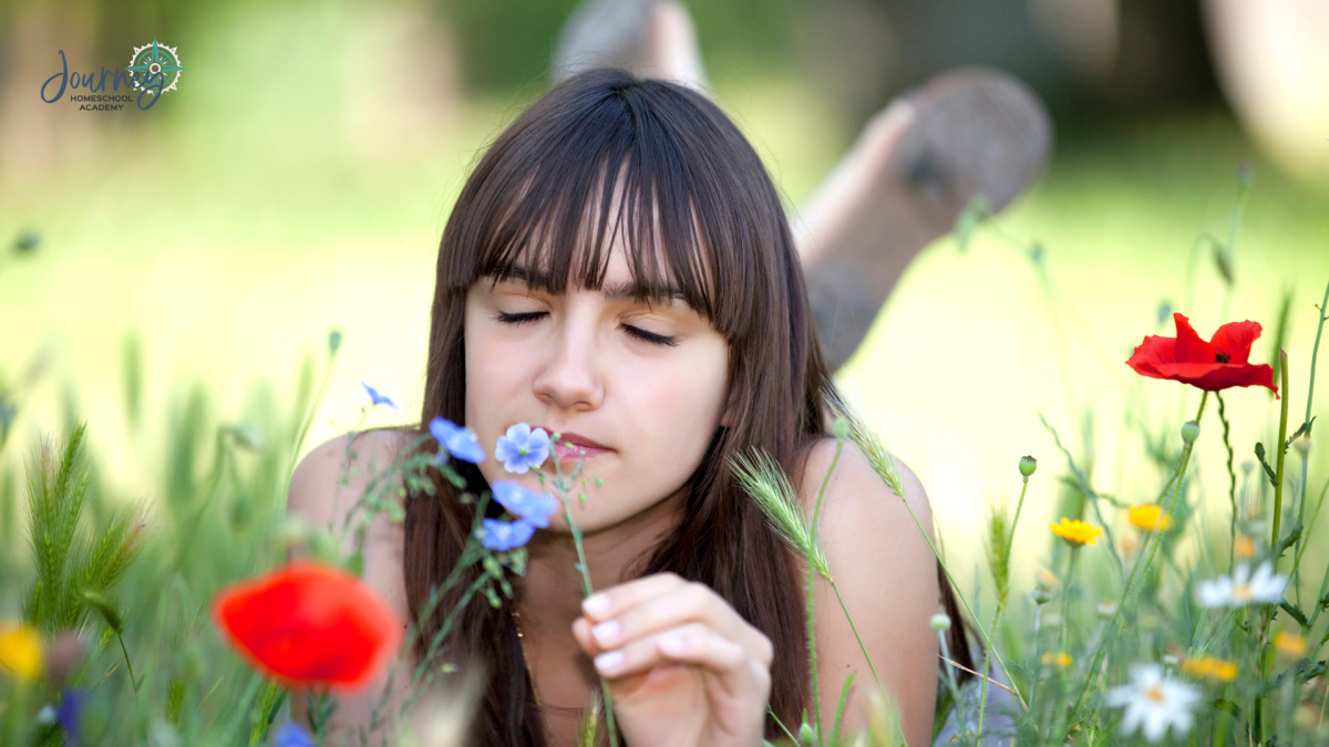 Teenage homeschool student smelling wildflowers in a meadow, illustrating the chemistry of smells and God’s design in the senses, from Journey Homeschool Academy.